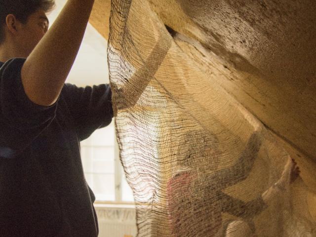 An die Dachschräge wird ein Flachsgewebe aufgetragen. | Foto: Hendrik Silbermann (ARTWORKs) Ein Teilnehmer hält ein Flachsgewebe fest, welches er an die Wandschräge anbringen wird. | Foto: Hendrik Silbermann (ARTWORKs)