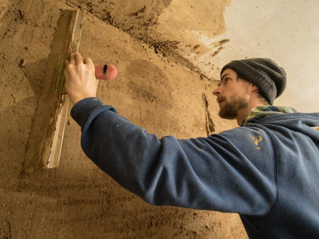 Glätten des aufgetragenen Lehmputzes mit einer Kardätsche. | Foto: Hendrik Silbermann (ARTWORKs) Ein Teilnehmer glättet den aufgetragenen Lehmputz mit einer Kardätsche. | Foto: Hendrik Silbermann (ARTWORKs)