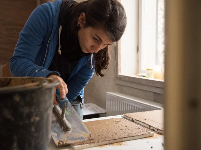 Testen von Lehmverhältnissen auf Musterplatten. | Foto: Hendrik Silbermann (ARTWORKs) Eine junge Frau testet verschiedene Lehmverhältnisse auf Musterplatten. | Foto: Hendrik Silbermann (ARTWORKs)