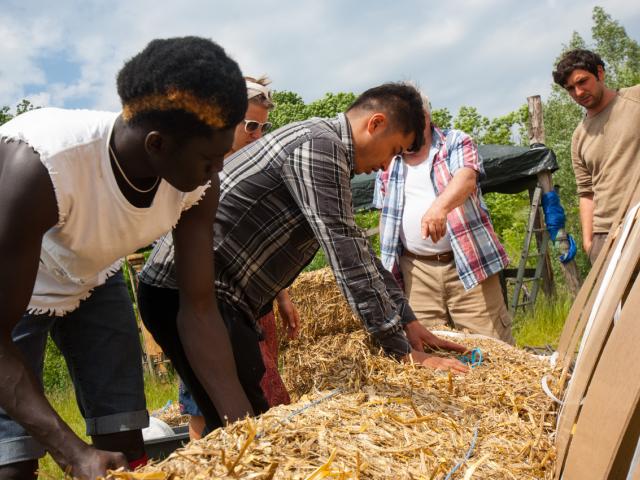 Gemeinsam werden die Strohballen von den Teilnehmenden auf der untersten Reihe befestigt. | Foto: Hendrik Silbermann (ARTWORKs) Die Teilnehmenden richten die Strohballen auf die Unterkonstruktion.