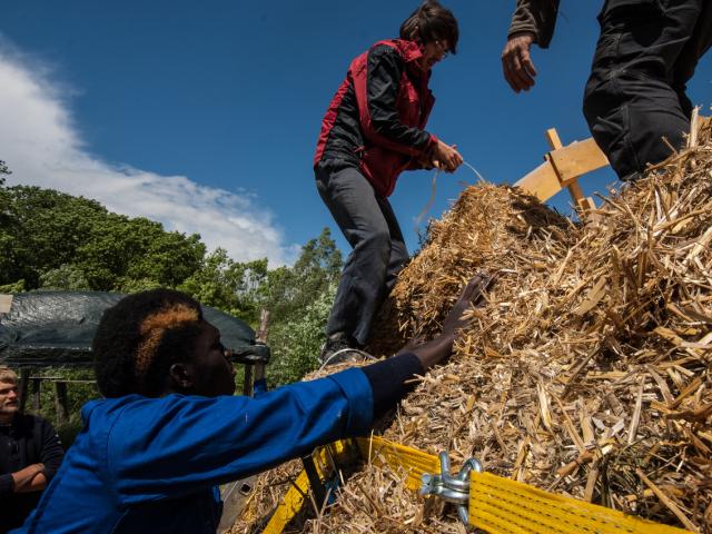 Alle packen beim Bau der Strohbrücke mit an. | Foto: Hendrik Silbermann (ARTWORKs) De Strohballen werden gemeinsam von den Teilnehmenden auf die Konstruktion getragen.